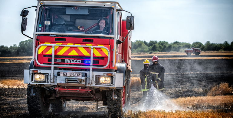 Camion citerne feux de forêt et ses deux sapeurs-pompiers achevant d'éteindre les restes fumant d'un feu de chaume.